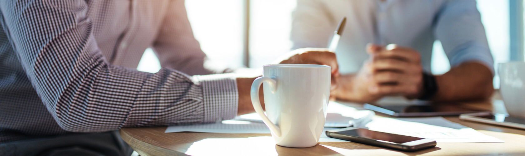 View of a table with coffee cup and documents and two arms