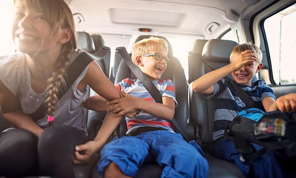 Three children in back seat of car, smiling and laughing
