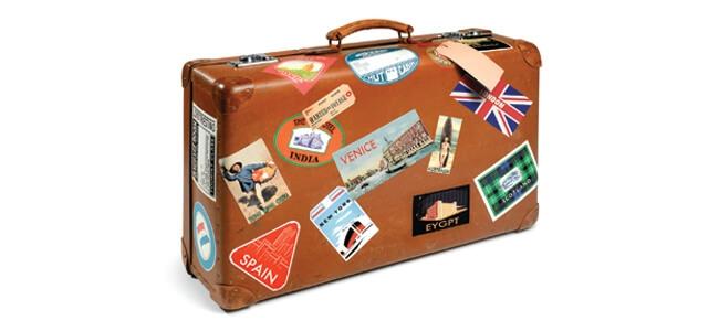 A brown suitcase covered with travel stickers from around the world