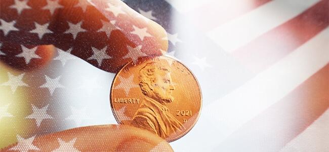 A 2021 penny is held by two fingers with American flag super-imposed