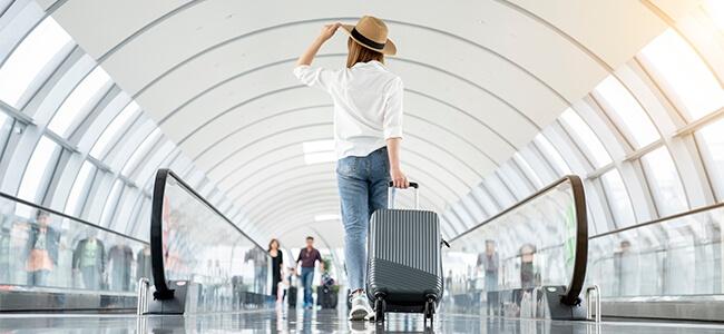 A woman wearing at travel hat walks through airport with suitcase