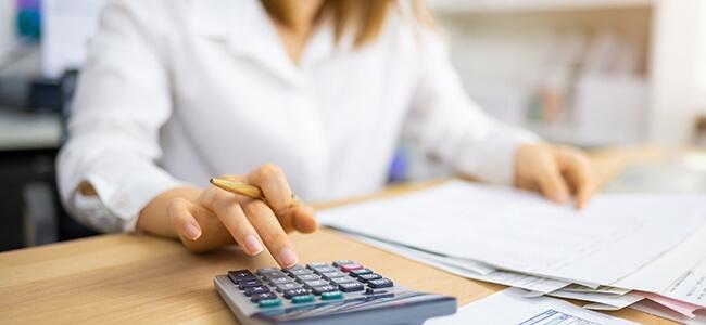 A woman sits at desk reviewing financial documents, using calculator
