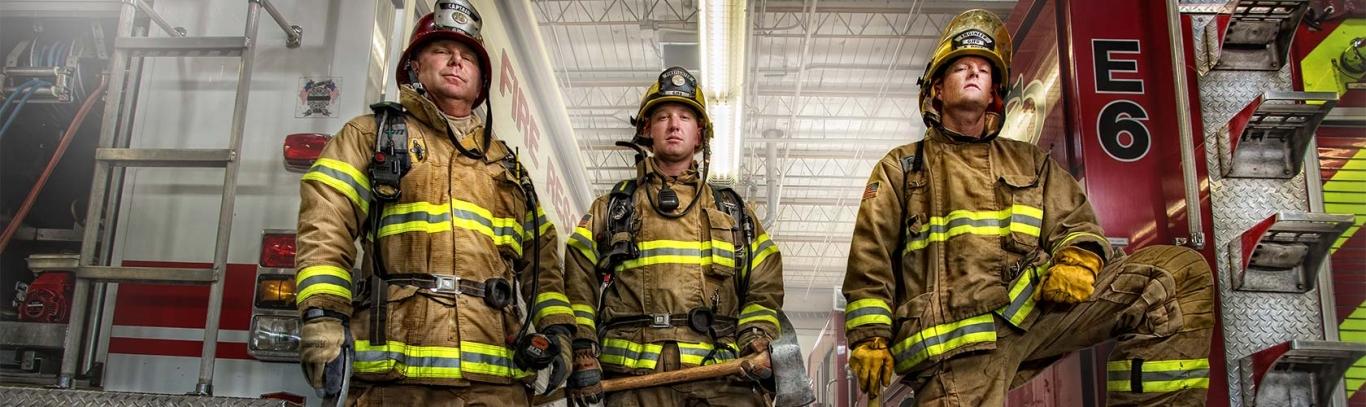 Three firefighters stand side by side in front of fire engine