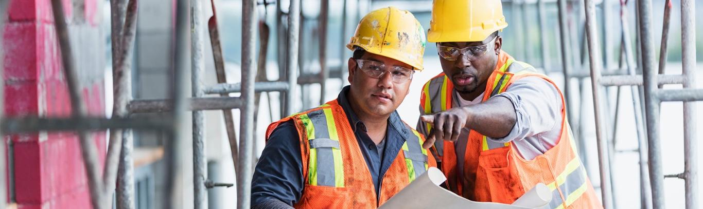 Two construction workers review blueprints at construction site