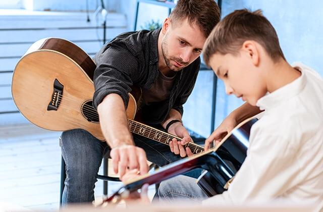 A guitar teacher works with a young student