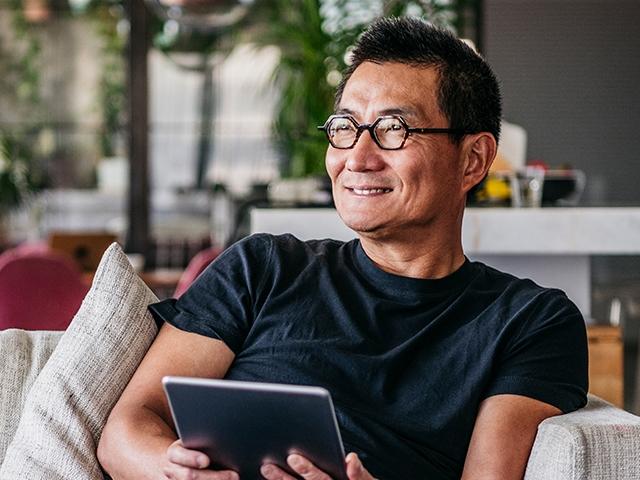 Man sits in living room using tablet and smiling
