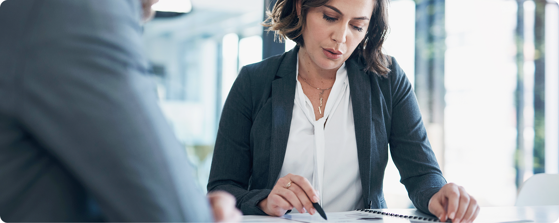 A woman sits with another individual, reviewing items in a book.