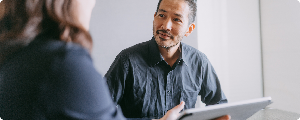 A man listens to a woman holding a tablet.