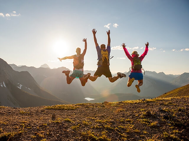 three skydivers float to earth with arms raised, sunset and mountains background