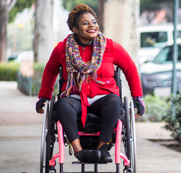 Woman in wheelchair smiling as she goes down the street