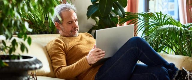 Man sitting on couch reviewing financial documents on tablet device