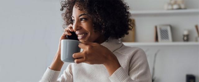 Woman smiling, drinking coffee while on a phone call