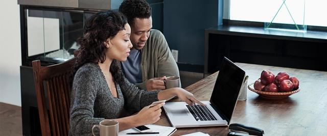 husband and wife sit in front of laptop reviewing finances