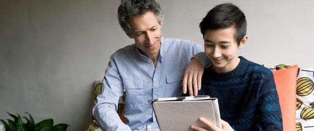 A father sits with son reviewing finances on a tablet device