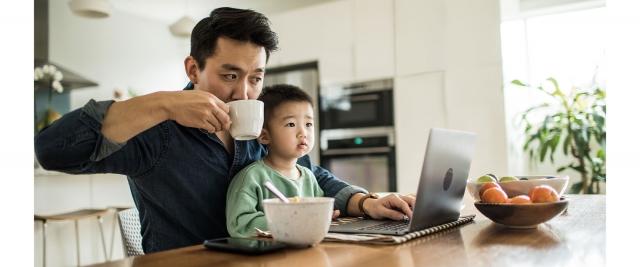 father and son sitting at kitchen table, father working on laptop