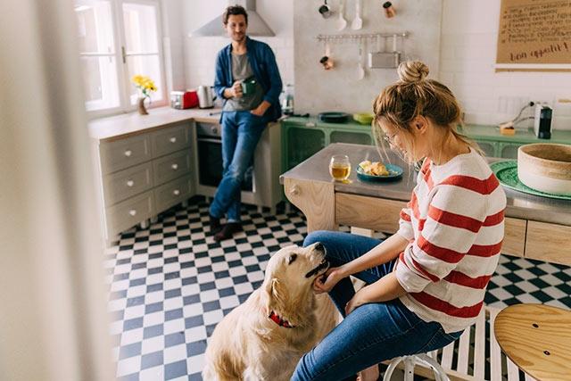 A husband and wife in kitchen drinking coffee and playing with dog