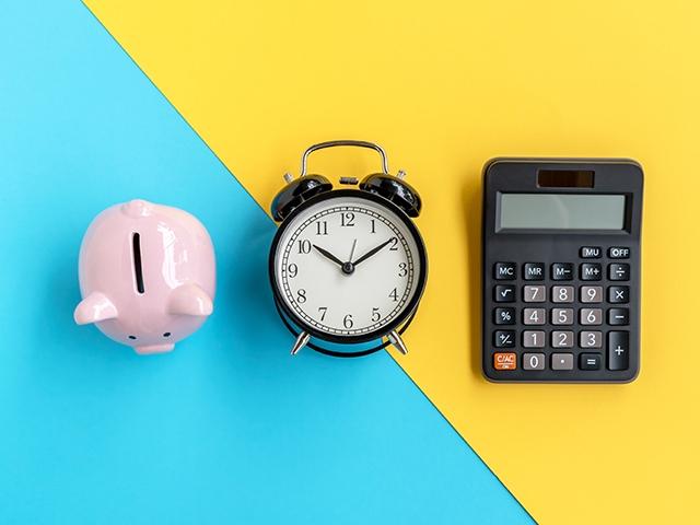 Top down view of a piggy bank, alarm clock and calculator sitting side by side