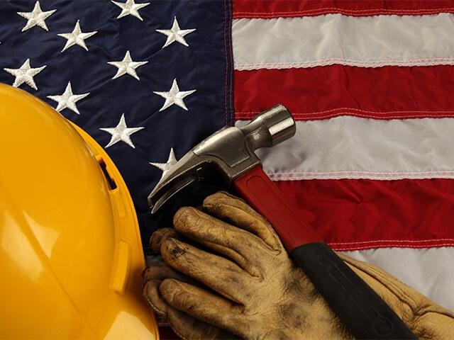 A hammer, hardhat and gloves rest on top of an American flag - Labor Day 2021