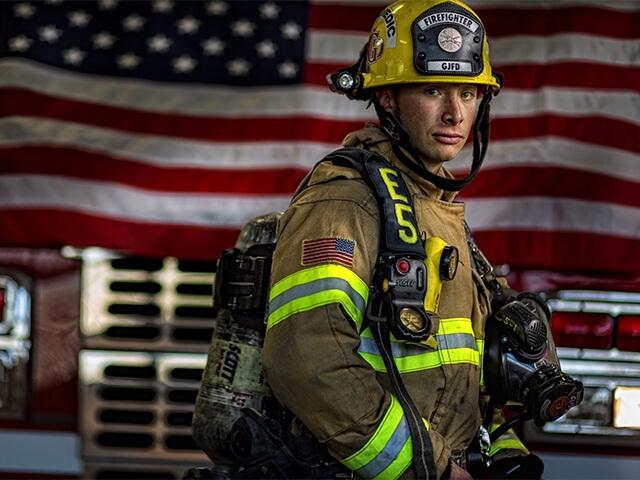 A firefighter stands in front of an American Flag. Empower Retirement