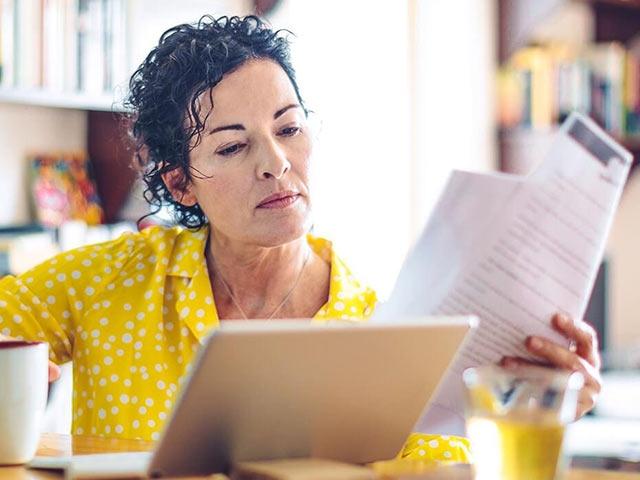 A woman at home reviews financial documents while having coffee