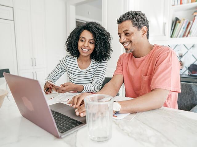 Husband and wife in kitchen reviewing financial information on laptop