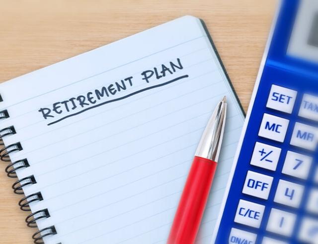 A calculator and pad of paper on a desk with written words: Retirement Plan 