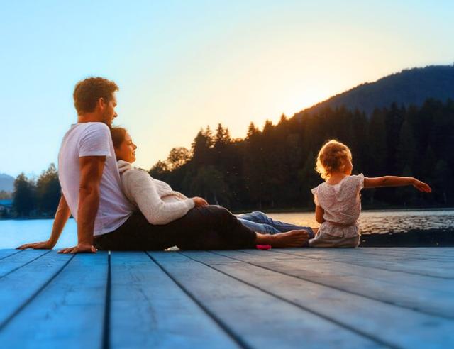 Father, mother and young daughter sit on dock overlooking lake