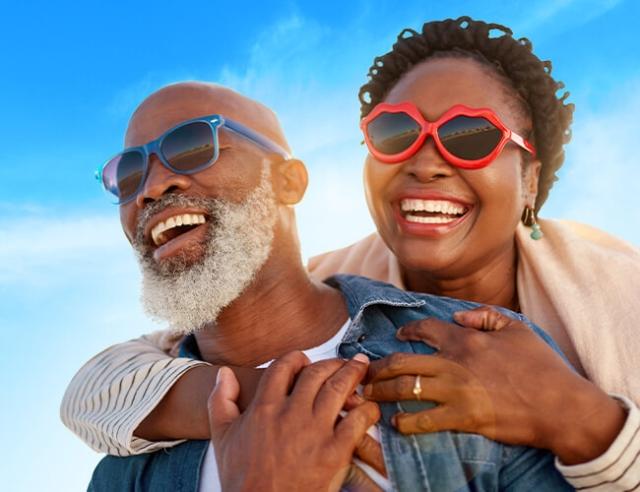 A wife embraces husband, both wearing sunglasses and laughing