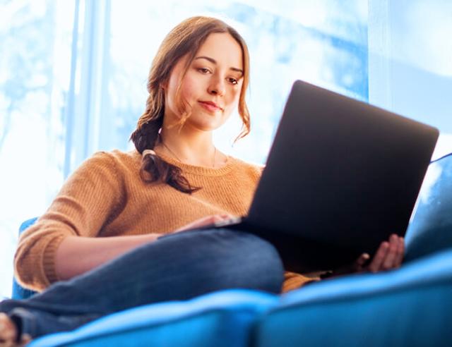 A woman sits on couch using laptop