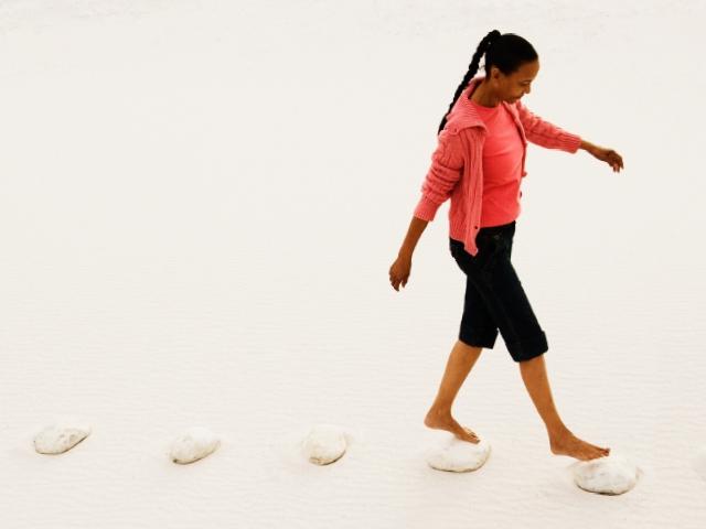 A woman walks on a beach stepping on stones 