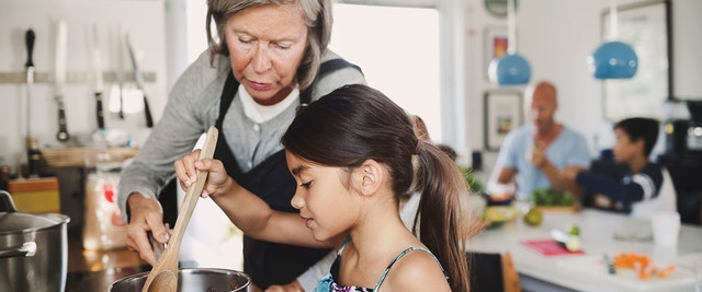 A woman with grey hair helps a young girl cook