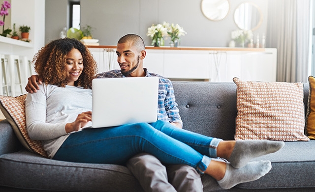 multi-racial couple sitting on couch, reviewing finances on laptop
