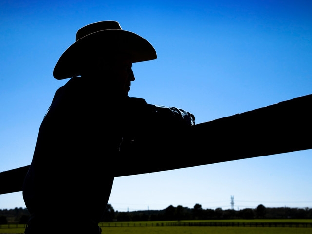 silhouette of a rancher leaning on a fence