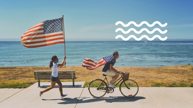 Girl runs with U.S. flag while friend rides bike along shoreline