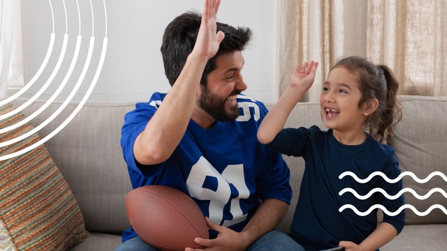 Father and daughter high five while cheering on their favorite football team. 