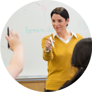 Teacher in a collared shirt holding a whiteboard marker, pointing next to the board