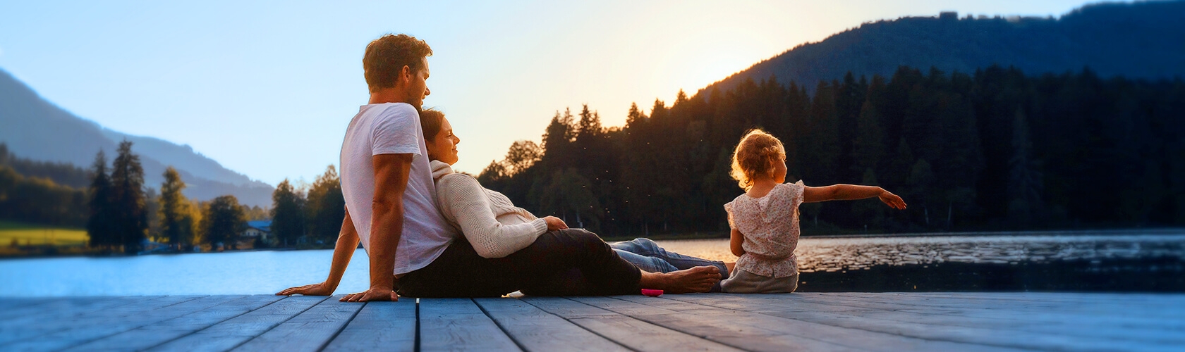 Father mother and young daughter sit on dock overlooking lake